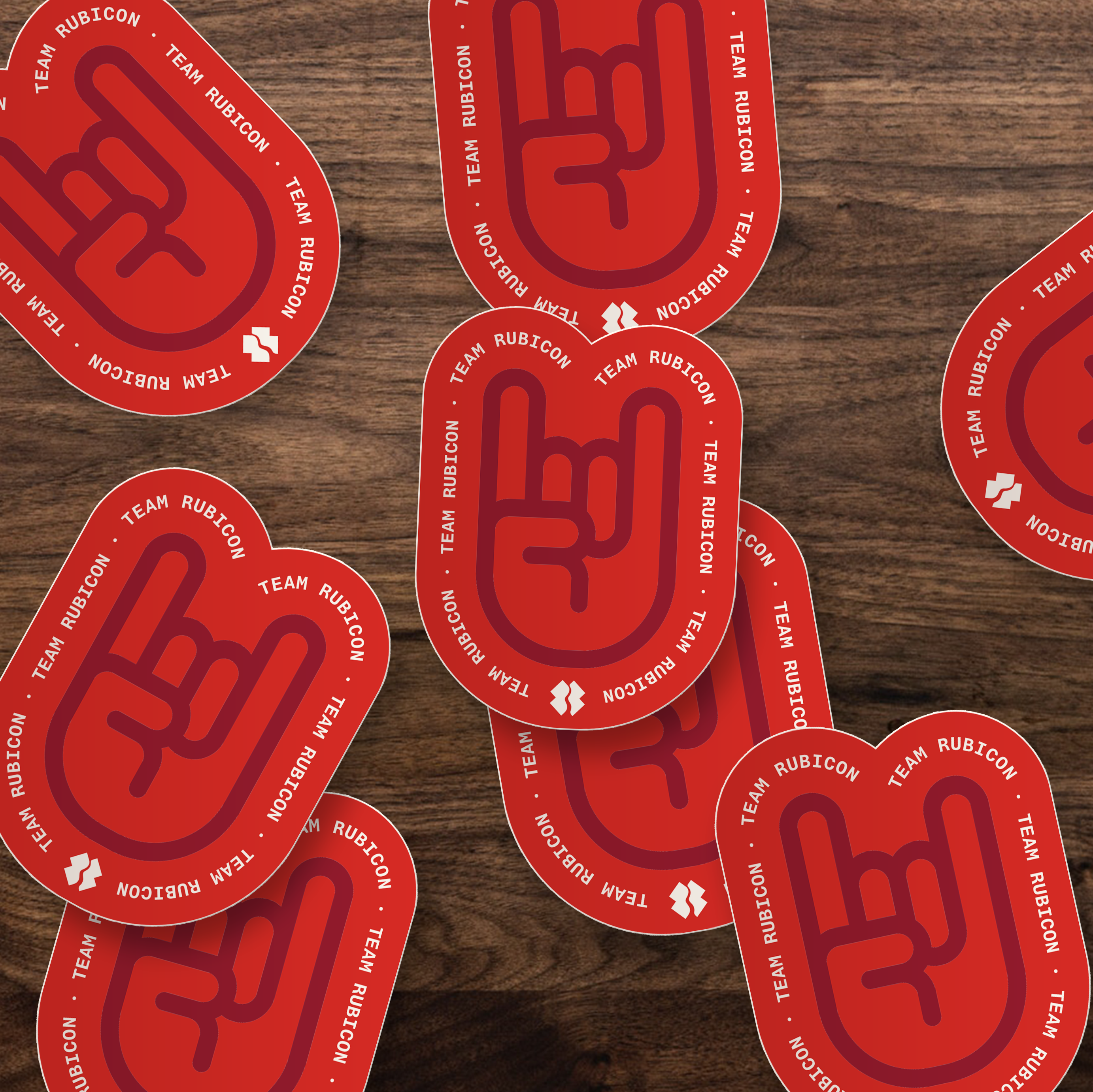 Red die-cut stickers with a stylized "ROCK ON" hand graphic and the text 'TEAM RUBICON' scattered on a dark wood surface.